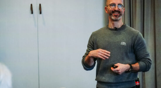 Et stort hvidt palæ med sort tag, centralt rundt tårn og flere skorstene, omgivet af træer og en stor, pænt klippet grøn græsplæne under en delvis overskyet himmel.